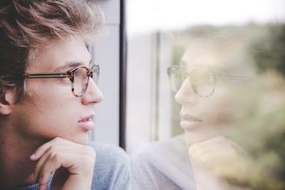 Man wearing glasses posing wile looking out a window with his hand on chin. - Don't let your illness define you